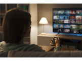 A woman sitting in front of a TV, holding a remote and looking through shows on Netflix